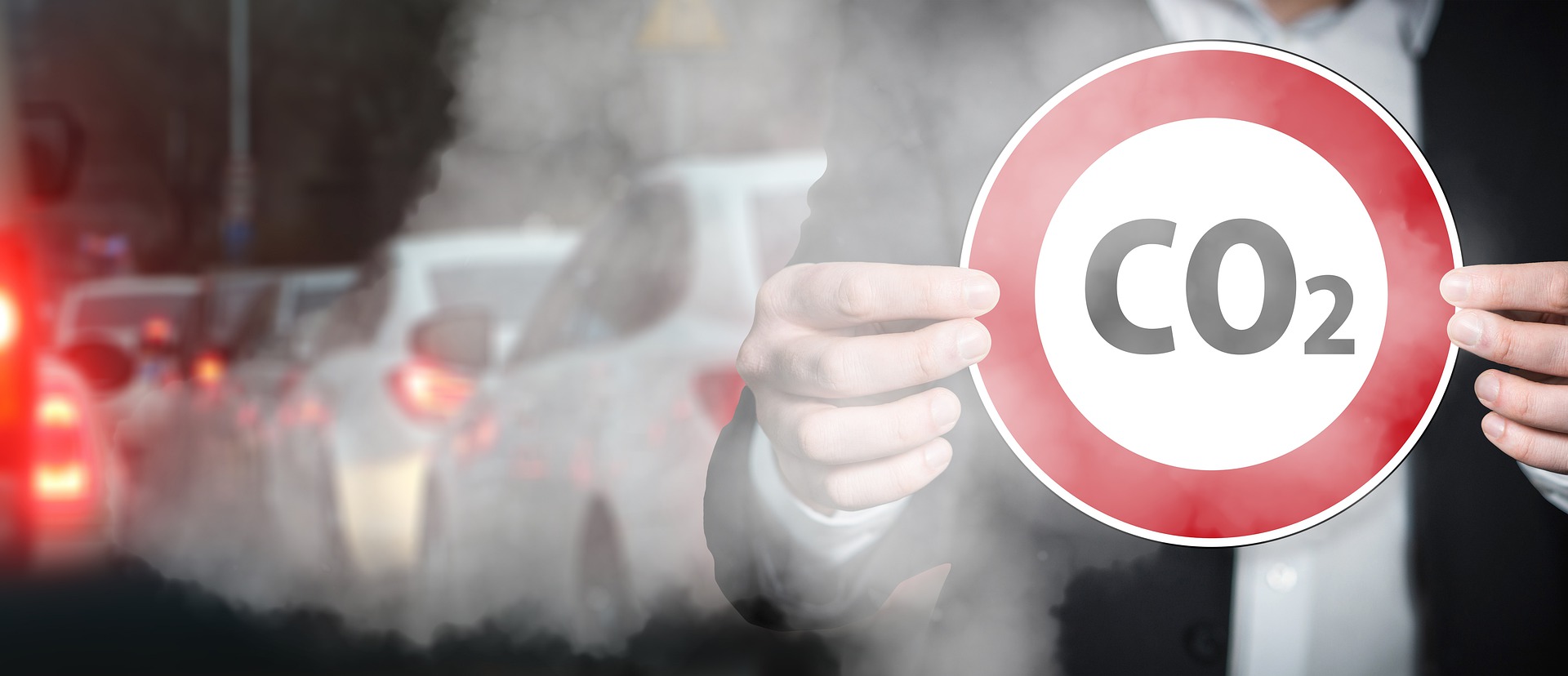 Mann in Anzug steht in Abgaswolke und hält rotes Stopp-Schild mit der Schrift CO2